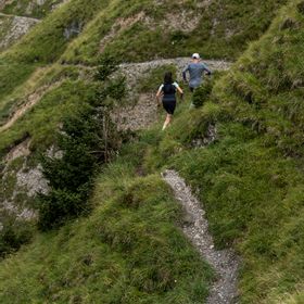 Eine Frau und ein Mann laufen in On Bekleidung und Schuhen einen Trail in Serfaus mit den Bergen im Hintergrund